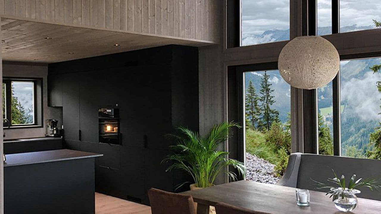Moderne hytte med sorte foringer rundt store glassvinduer og trepanel på veggene.