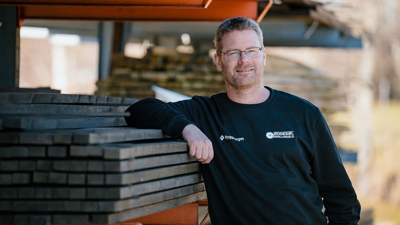 Byggtorget ansatt som lener seg på hylle med terrassebord.