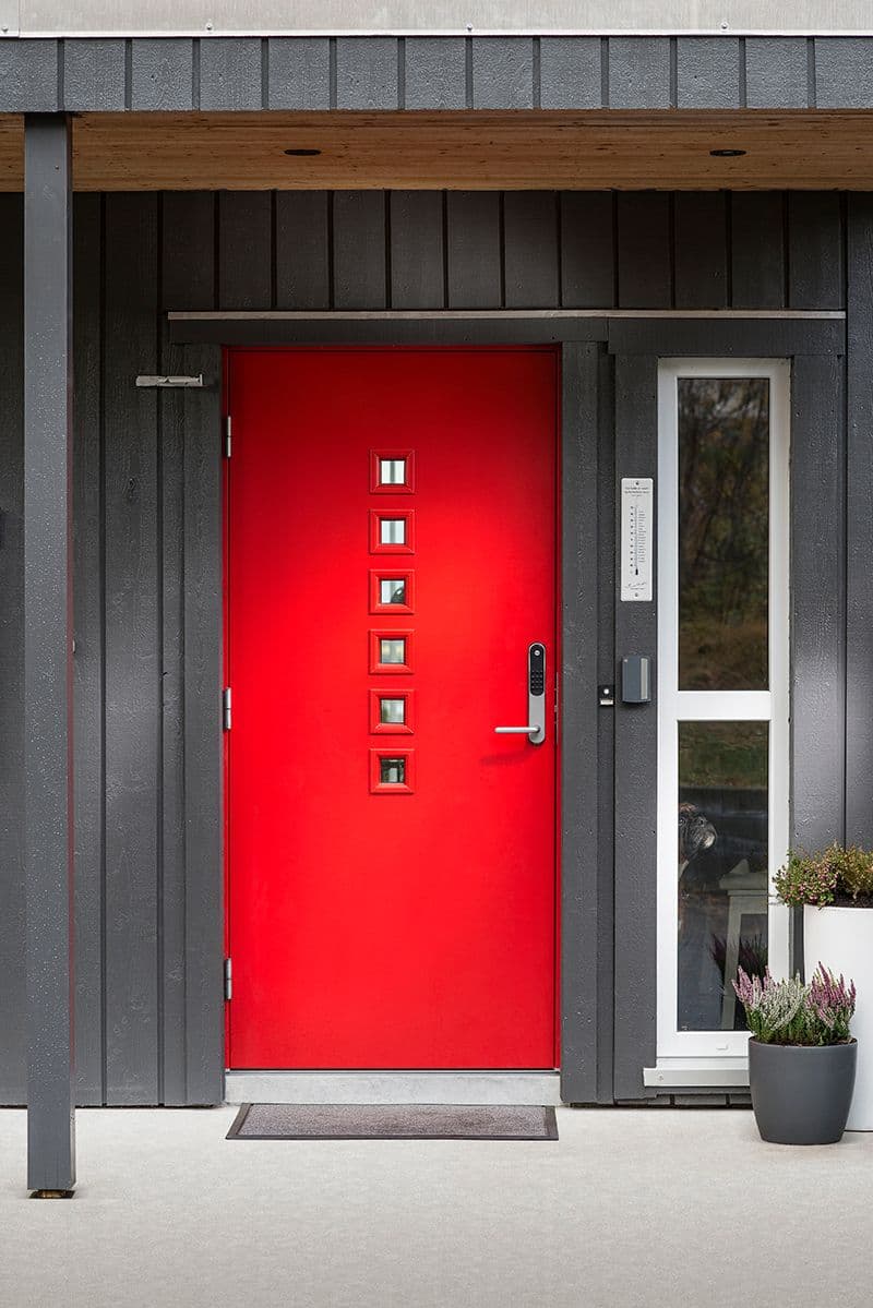 Rød ytterdør på grått hus.