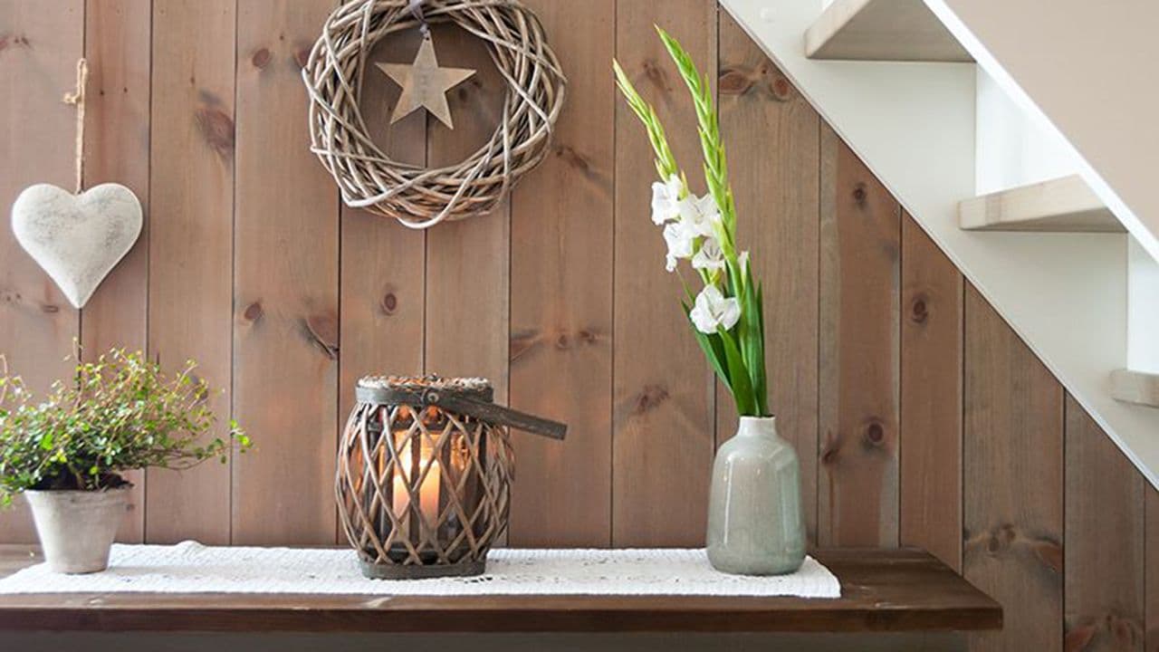 Beiset trepanel på hytte bak en grønn kommode med pyntegjenstander.