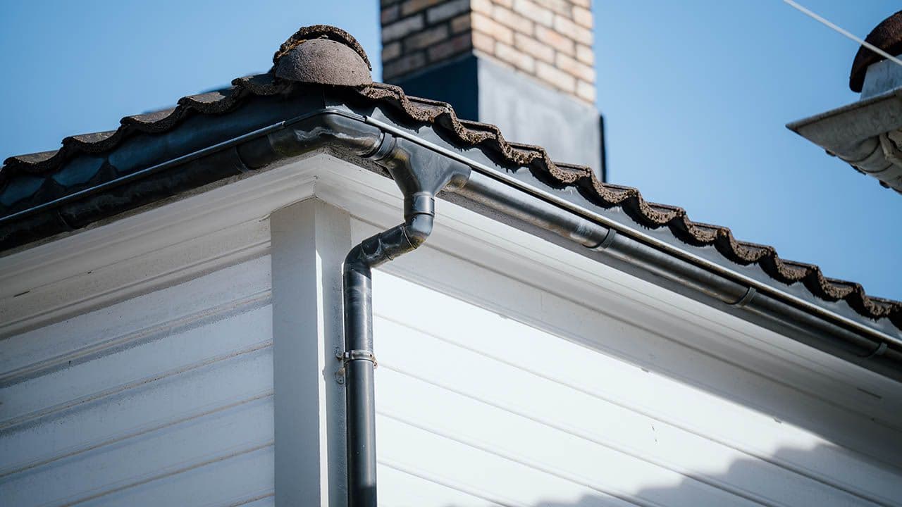 Sort takrenne på hvitt hus med sort takstein.