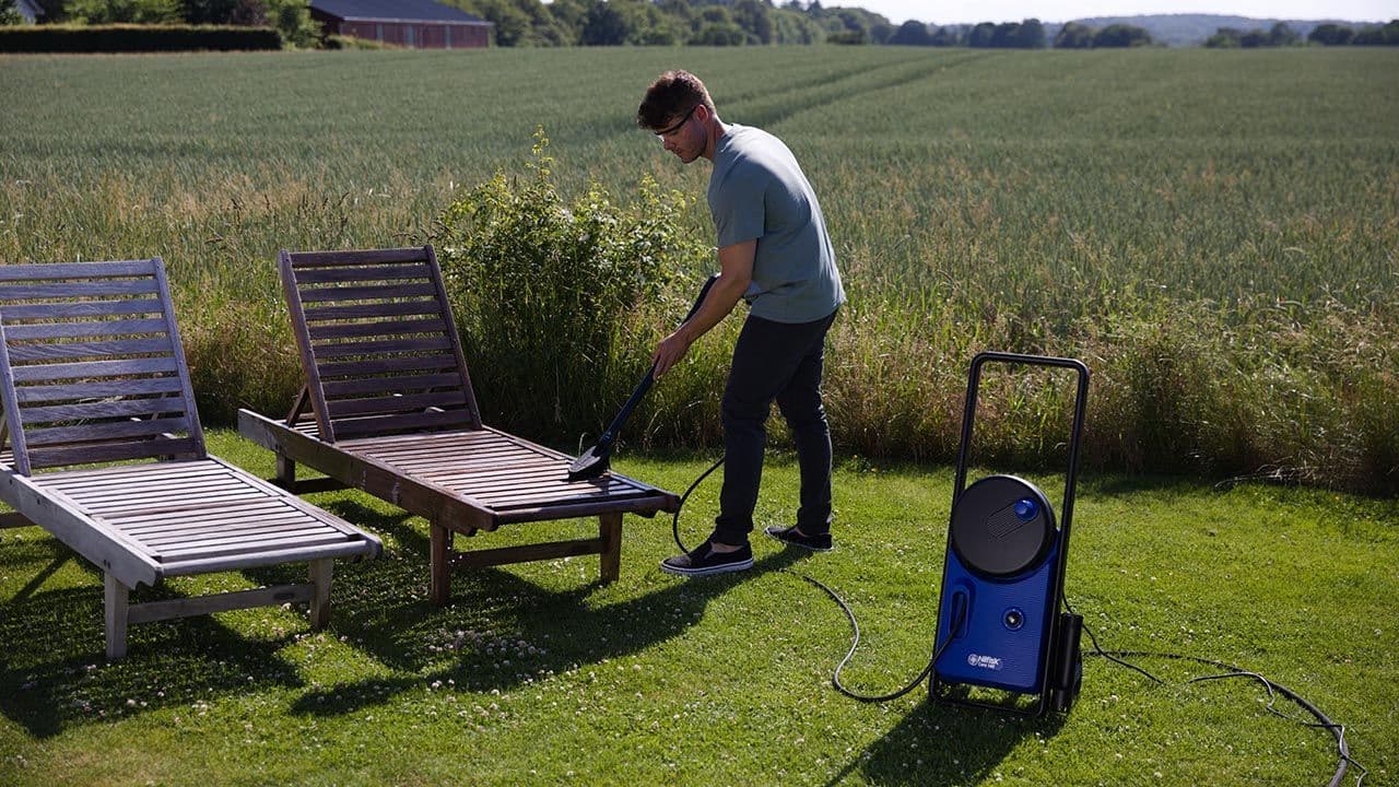 En mann vasker utemøblene med Nilfisk produkt