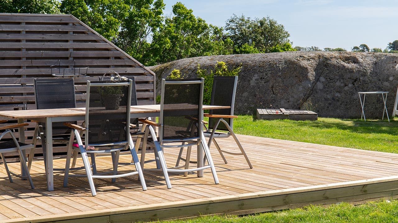 Trykkimpregnert terrasse med grånet levegg og spisebord.