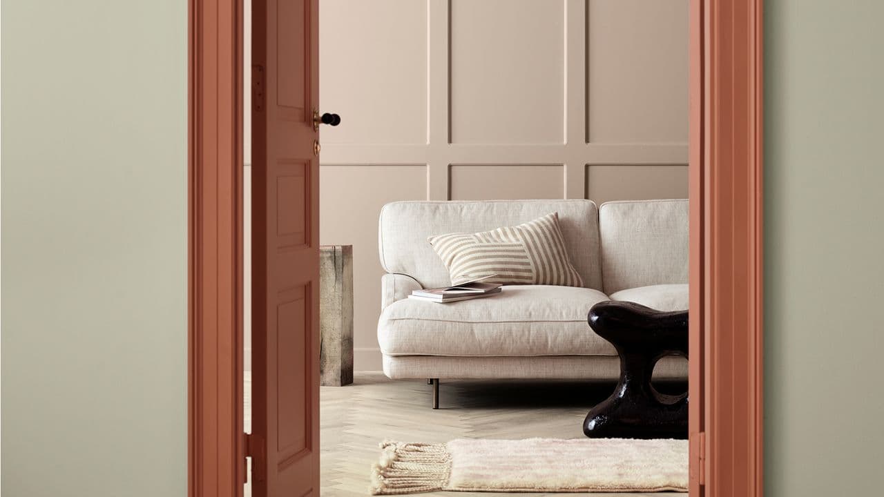 Stue med hvit sofa som du ser gjennom en døråpning hvor lister og dør er malt med 20217 Muted Coral fra Jotun.