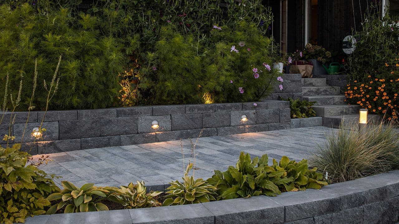 Norsk hage med utebelysning i mur som er blomsterbed.